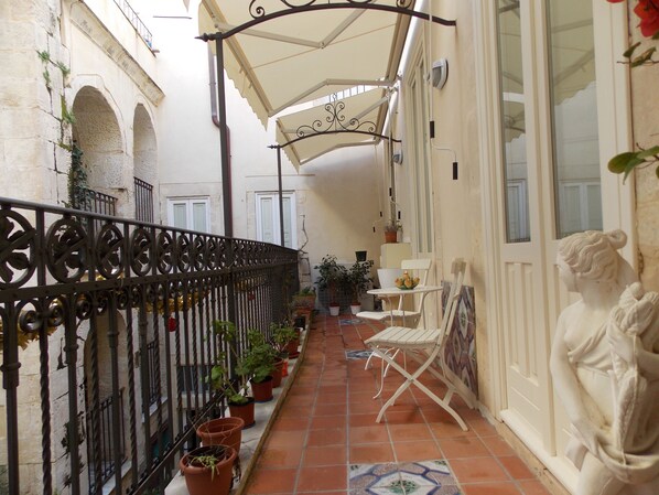 A narrow corridor with a tiled floor, potted plants, a white chair, and a statue.