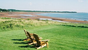 En gräsyta med trästolar som är placerade så att de vetter mot en strand.