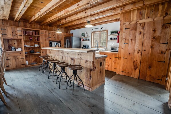 Un interior de madera con una zona de bar, taburetes y una cocina con armarios y electrodomésticos de madera.