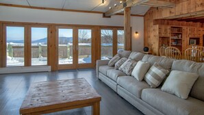 Un salón amplio con un sofá grande, una mesa de centro de madera y vistas a un paisaje nevado a través de puertas de cristal.