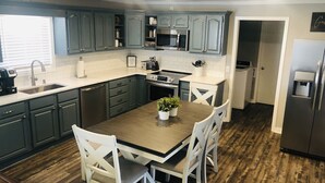 Une cuisine moderne avec des meubles de couleur sombre, une table à manger en bois et des chaises blanches.