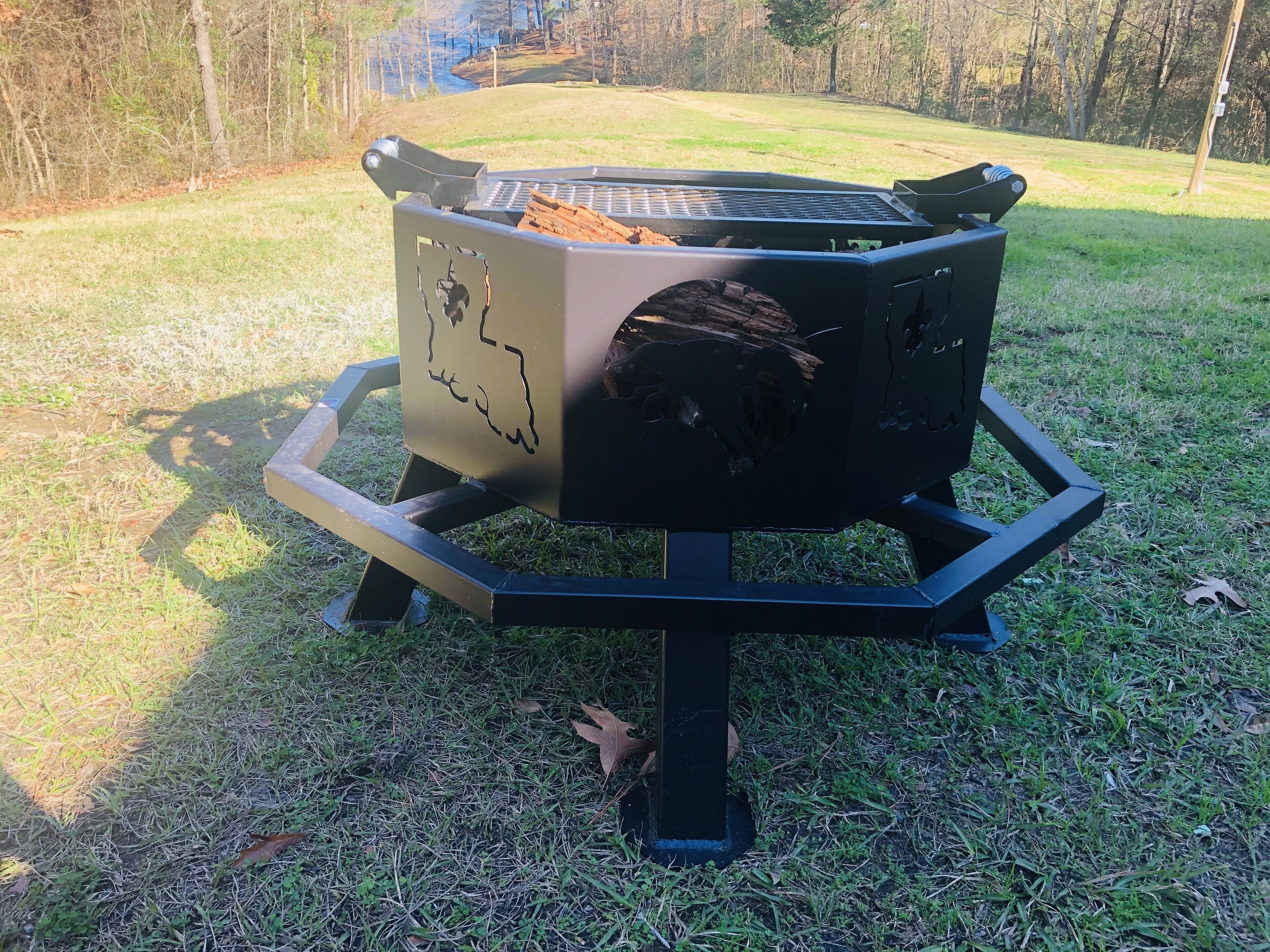 A portable grill with a metal grate and a logo, placed on a grassy area.