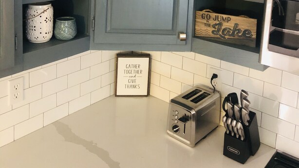 Une cuisine avec des meubles de couleur bleue, des carreaux blancs, un grille-pain et divers objets de décoration.