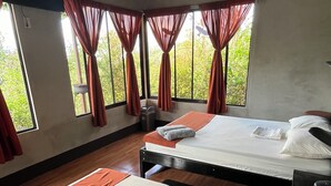 A room with two beds, a window with curtains, a small trash bin, and a ceiling fan.