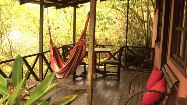 A wooden deck with a hammock, a table, and chairs.