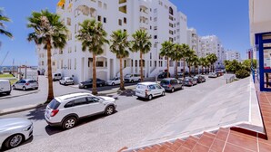 Un immeuble blanc à plusieurs étages, doté de balcons, avec des voitures garées et des palmiers.