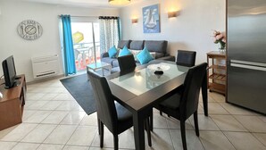 Une cuisine moderne équipée d’un réfrigérateur, d’une table à manger et de chaises. On y trouve également un canapé avec des coussins, une horloge au mur et un tableau.