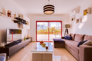 A modern living room with a flat-screen TV, glass coffee table, sofa, and a red-framed sliding door leading to an outdoor area.