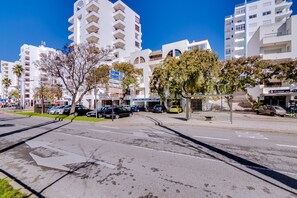 A street view with modern buildings, parked cars, and a clear blue sky.