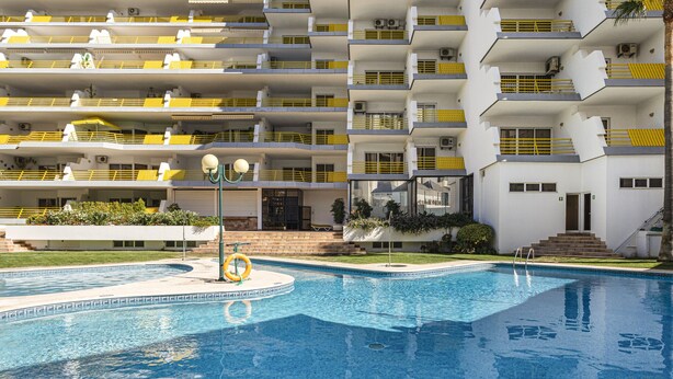 Een modern hotel met een zwembad, meerdere balkons en een verzorgde tuin.