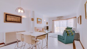 Een moderne woonkamer met een eethoek, met een witte eettafel, stoelen, een bank en een televisie.