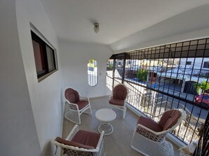 A balcony with white wicker chairs, a small round table, and a view of the street through a barred window. - 6B SANTIAGO CENTER, GREAT COZY HOUSE APT. TO STAY (Altos de Vireya)