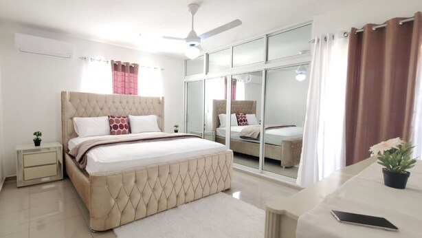 Un dormitorio con una cama grande, una mesita de noche y un ventilador de techo, con un ventanal corredero que da a otra habitación.
