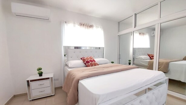 A modern bedroom with a large bed, bedside tables, a wardrobe, and a mirror.