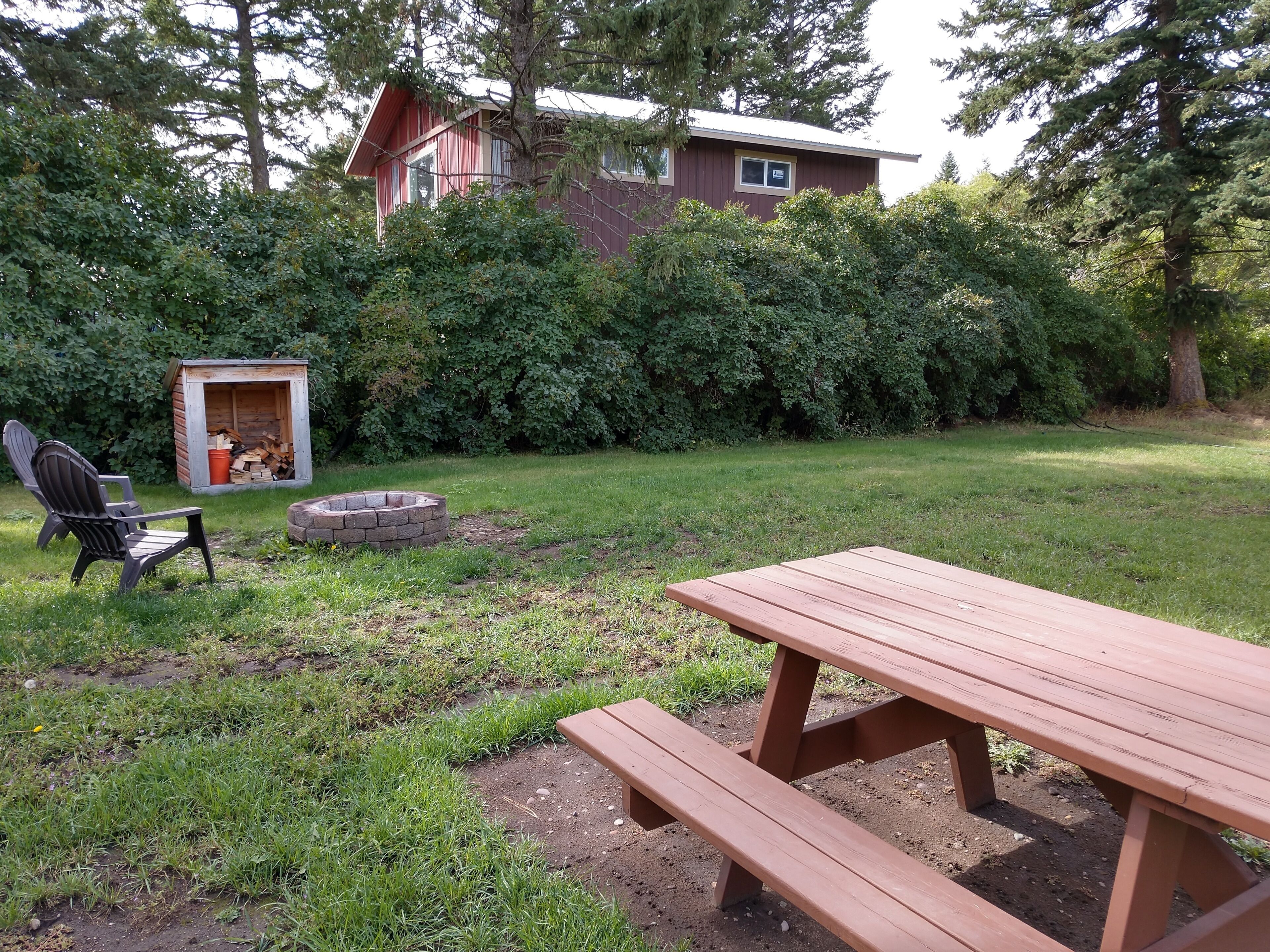 Ein Garten mit einem Holztisch, einem Feuerkorb, einer Gartenhütte und einem Stuhl.