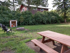 A backyard with a wooden picnic table, a fire pit, a shed, and a chair. - Beautiful cabin close to Glacier Park, Flathead Lake & Whitefish Mountain. (Columbia Falls)