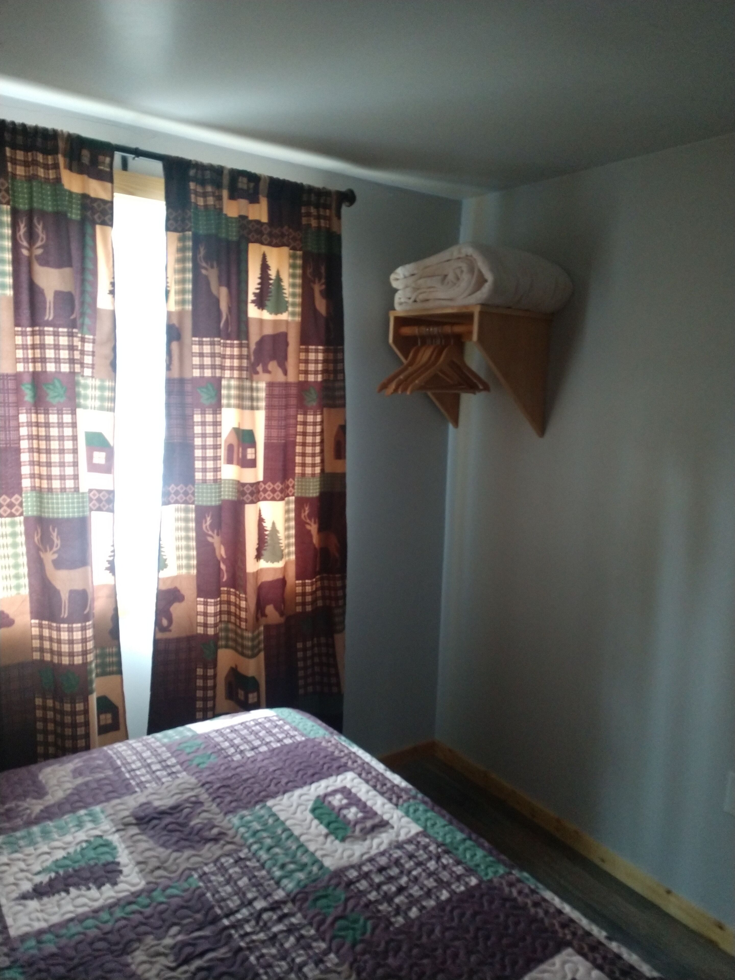 Una habitación con una cama, una ventana con cortinas y un estante en la pared con toallas dobladas.