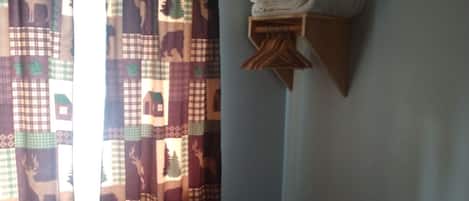 Una habitación con una cama, una ventana con cortinas y un estante en la pared con toallas dobladas.