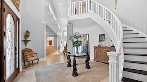 Un hall espacioso con una imponente escalera, una chimenea decorativa y un espejo grande.