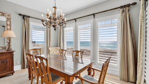 Comedor con una mesa grande y sillas, un candelabro y ventanas amplias con vista a la playa.
