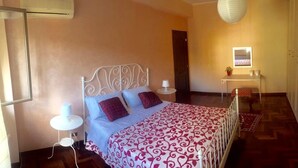 A bedroom with a metal bed frame, a patterned bedspread, two bedside lamps, a small table with a plant, and a mirror on the wall. - Island 92100: beautiful house in the heart of Agrigento (Agrigento)