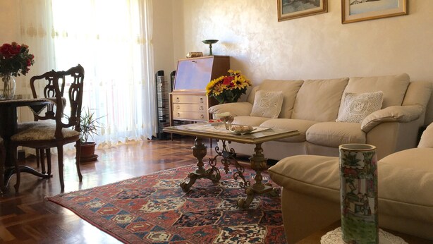 A living room with a sofa, a coffee table, a patterned rug, a vase with flowers, and a cabinet with books. - Island 92100: beautiful house in the heart of Agrigento (Agrigento)