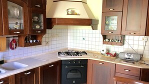 A kitchen with wooden cabinets, a gas stove, a black oven, and a dining area with a table and chairs. - Island 92100: beautiful house in the heart of Agrigento (Agrigento)