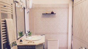 A bathroom with a bathtub, a sink, a mirror, a towel rack, and a shelf with toiletries. - Island 92100: beautiful house in the heart of Agrigento (Agrigento)