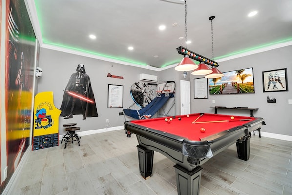 A pool table with a red felt surface, a hanging light fixture, and a poster of Darth Vader.