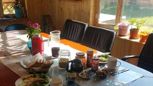 A dining table set with food, drinks, and condiments in a room with wooden walls and a window. - Mountain View Guesthouse (Moron)