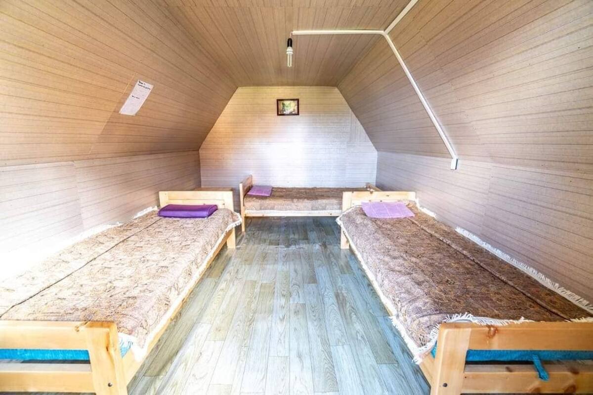 A small attic room with wooden walls and sloped ceilings. There are three wooden beds with blue and purple bedding.