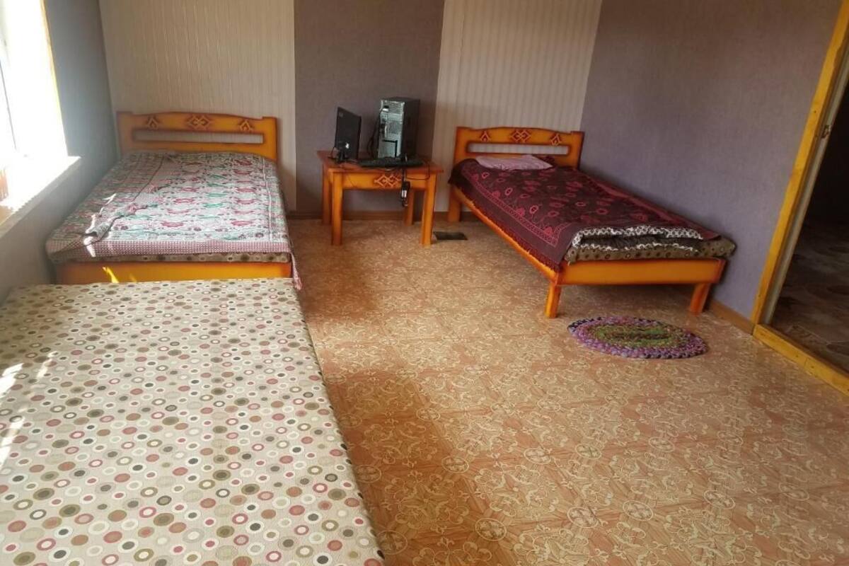 A room with two beds, a small table with a computer, and a patterned carpet.