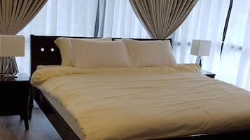 A large bed with a wooden frame, two bedside tables with lamps, and sheer curtains.