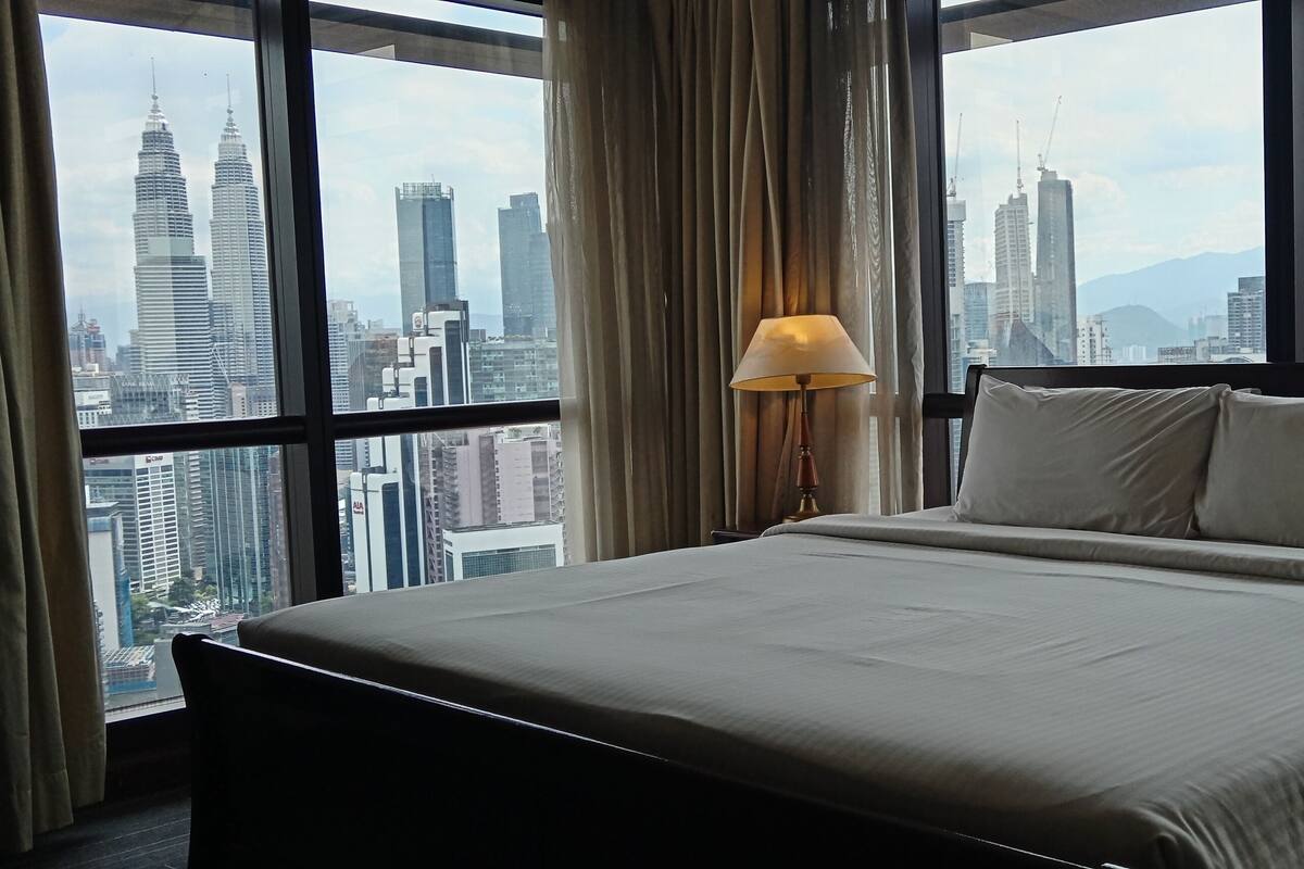 Une chambre d’hôtel avec un grand lit, une lampe et une vue sur un paysage urbain avec de hauts immeubles.