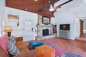 A living room with a fireplace, a television, and a ceiling fan.