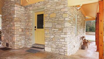 A stone building with a yellow door, a covered porch with wooden chairs, and a concrete floor.