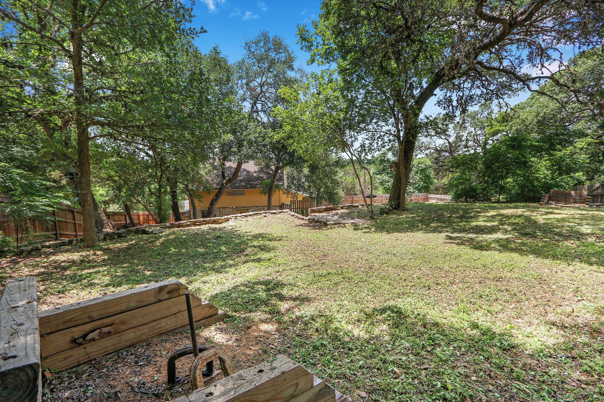 A fenced outdoor area with a wooden bench, trees, and a building in the background.