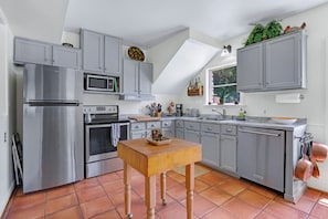 A modern kitchen with grey cabinets, stainless steel appliances, and a wooden table.