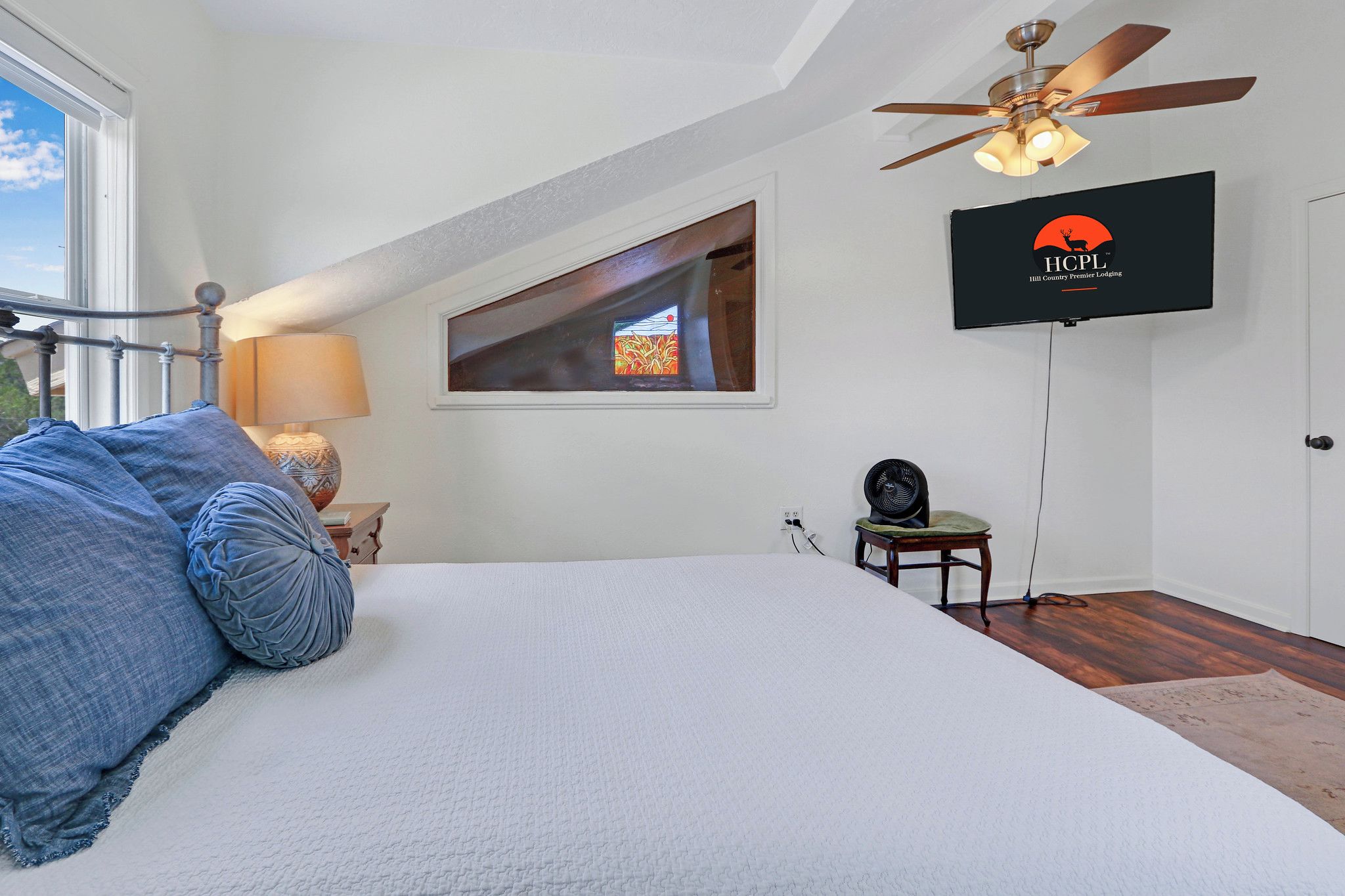 Une chambre à coucher avec un lit, un ventilateur de plafond, une télévision et une fenêtre.