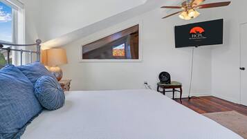Une chambre à coucher avec un lit, un ventilateur de plafond, une télévision et une fenêtre.