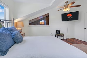 A bedroom with a bed, a ceiling fan, a TV, and a window.