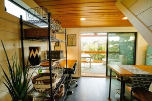 A modern kitchen with a wooden ceiling, a dining area with a table and chairs, and a view of the outdoors through a glass door. - Bluebonnet ↠ Cabin with view and Pro Coffee Setup, Pickleball (Wimberley)