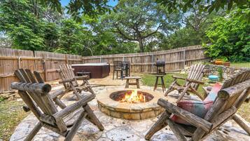 Une terrasse extérieure avec un foyer en pierre, des chaises en bois, une table et un barbecue.