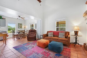 A living room with a brown leather sofa, a blue ottoman, a patterned rug, and a wooden coffee table. - Mi Rancho- 2 bed/2 bath-Hot tub, Fire pit, and Pinball machine! (Wimberley)