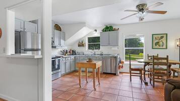 Une cuisine moderne avec un coin repas, comprenant un îlot central, des meubles de cuisine blancs et un ventilateur de plafond.