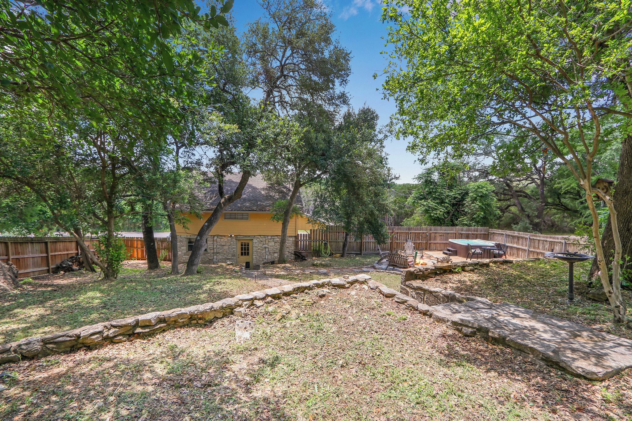 A backyard with a stone wall, a wooden deck, and a yellow house.