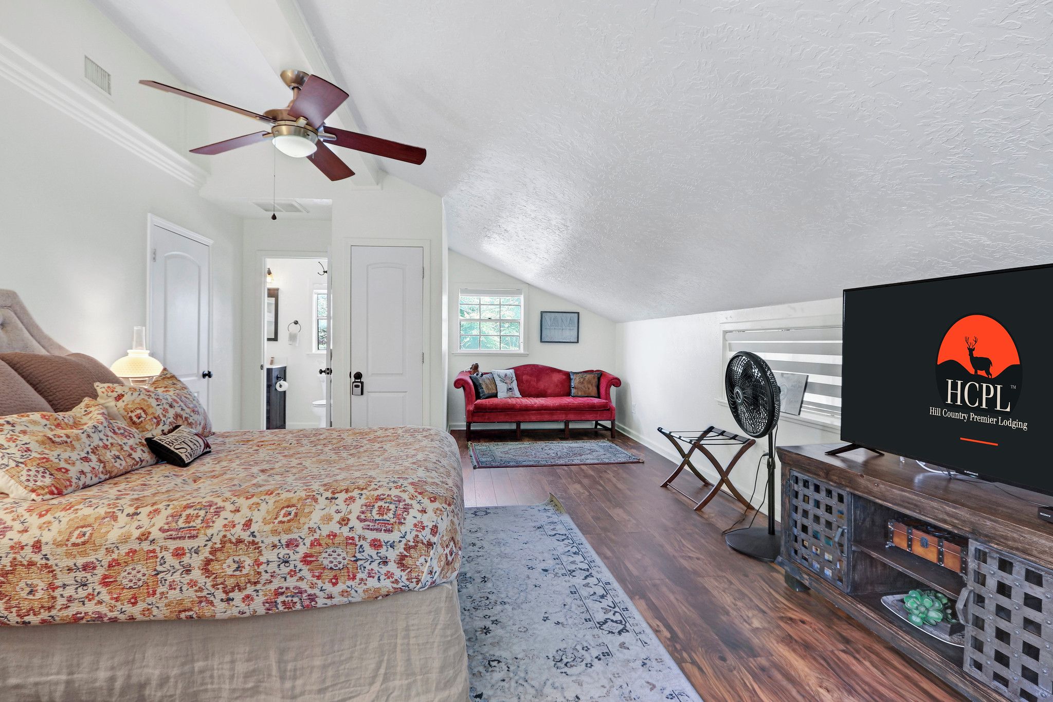 A bedroom with a bed, a ceiling fan, a red sofa, a TV, and a wooden cabinet.
