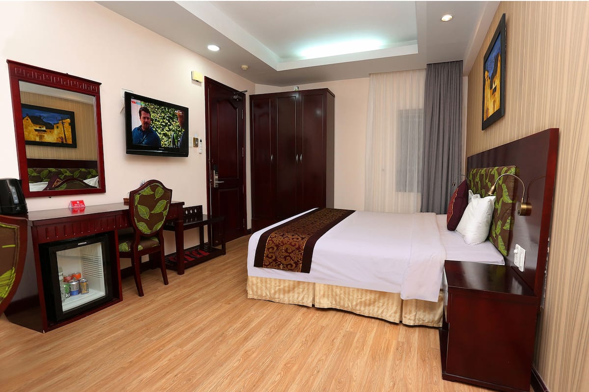 Una habitación de hotel con cama, escritorio con computadora, armario y un refrigerador pequeño.