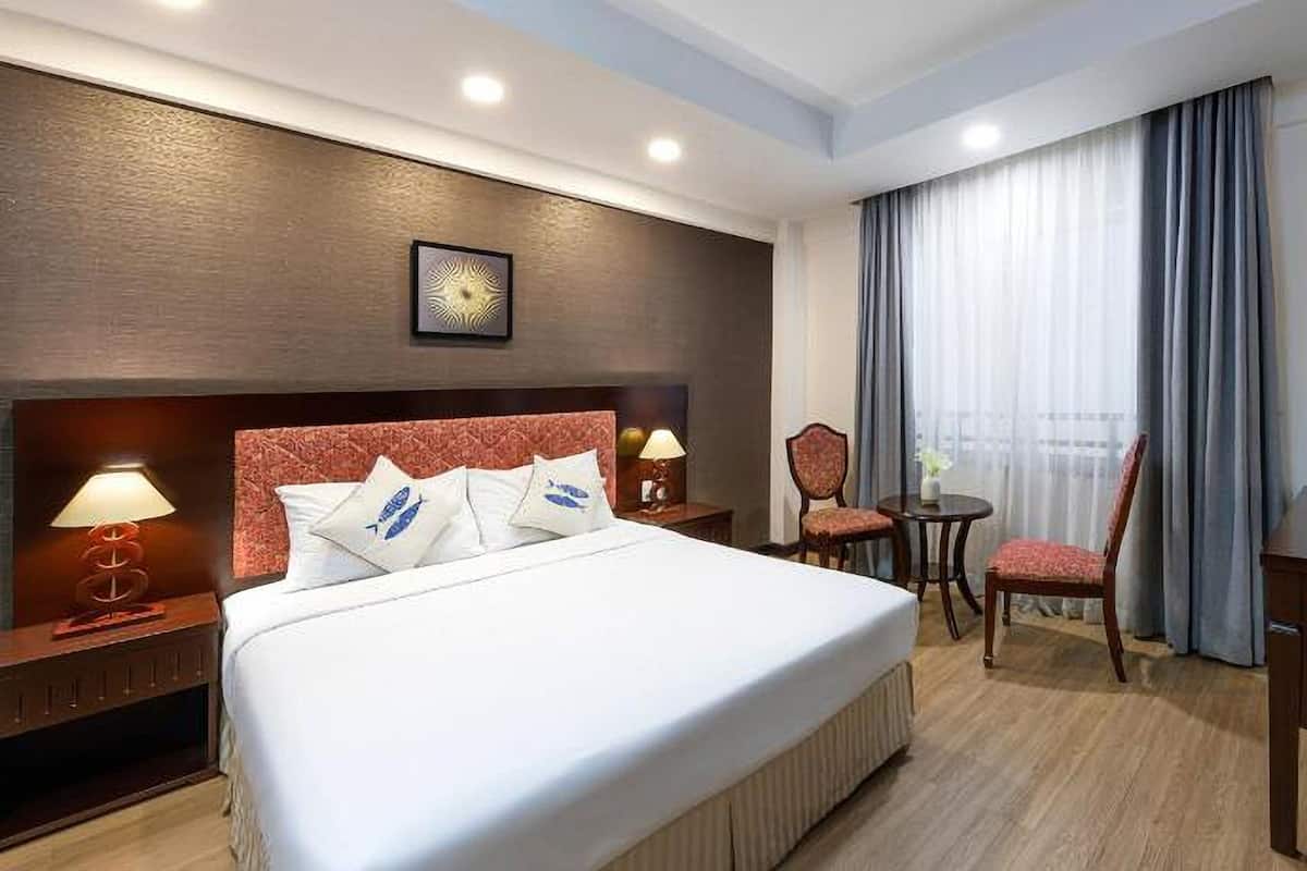 Una habitación de hotel con una cama grande, dos mesitas de noche con lámparas, un escritorio, una silla y un televisor.