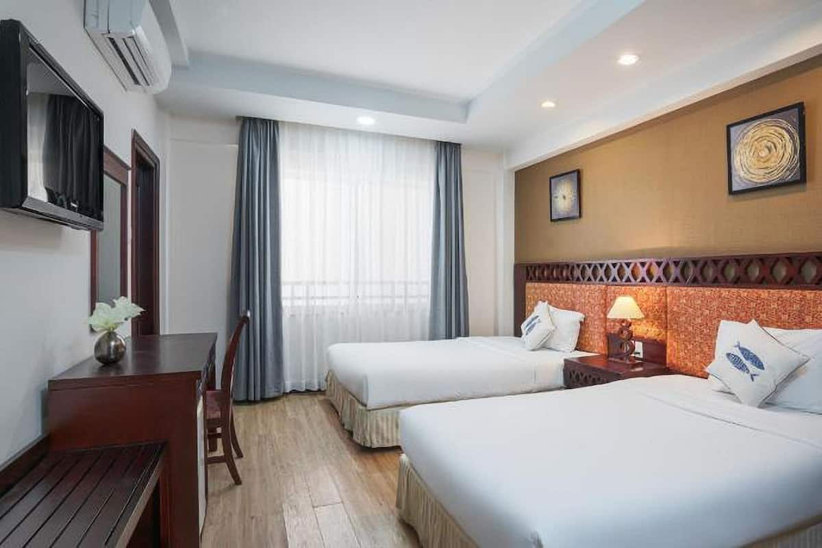 Habitación de hotel con dos camas, un escritorio, una silla, una lámpara y una ventana con cortinas.